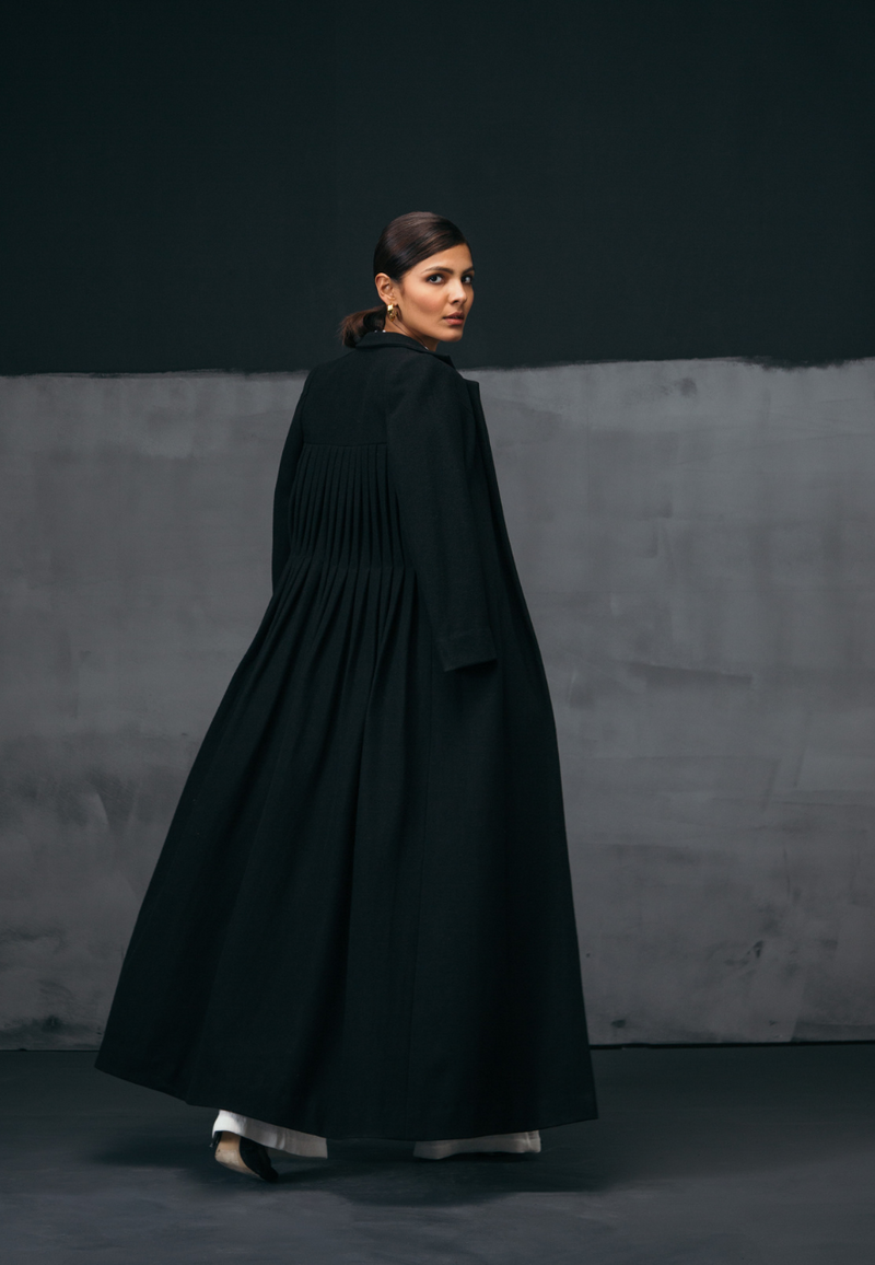 Mannat Gupta's collection of women's coats and jackets. This black collared wool coat comes with pleating on the back creating depth and movement in the piece. The wool coat is floor-length making it perfect to be paired with long dresses and formal attire in the fall and winter. Pair this with a flared pant and top or sweater along with booties and minimal gold jewelry to complete the look