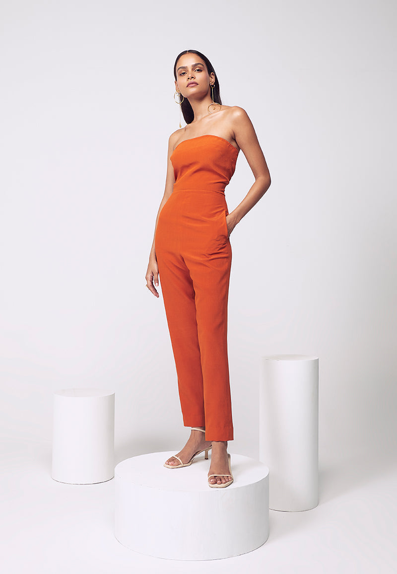 New style figure-hugging jumpsuit. Crafted in pure silk crepe in burnt orange with inseam pockets which are perfect for your next soiree or even a beach party. Easy to wear this ankle-length bodycon jumpsuit comes with a detachable pleated trail with a hook and eye closure for easy access and confort. Create multiple looks for multiple events with detachable, functional clothing. Complete the look with heeled sandals and minimal gold jewelry.