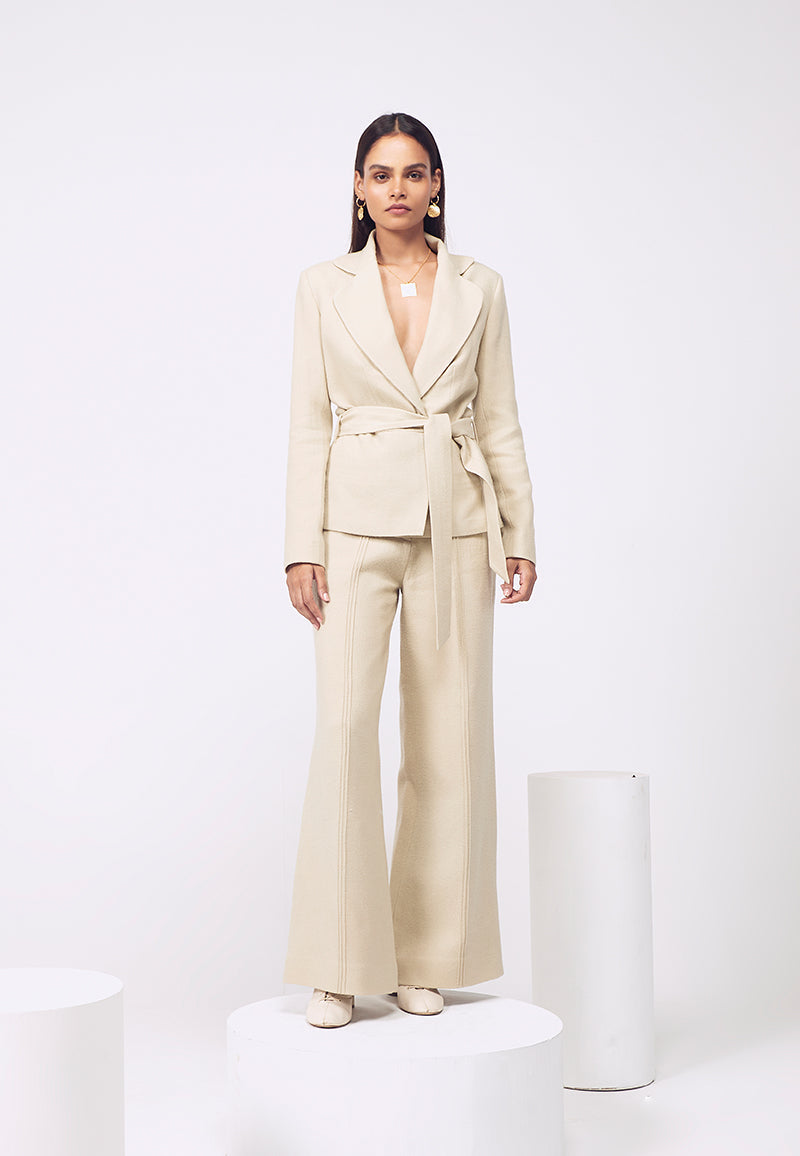 Slip into this neutral boned wrap wool co-ord set for fall or winters. Crafted using plush wool, this beige wrap around jacket with belt adds shape to the piece. High-waisted flared wool pants with tuck details are sure to grab attention. Pair it with heels or booties with minimal god jewelry for work or an evening soiree or a dinner.