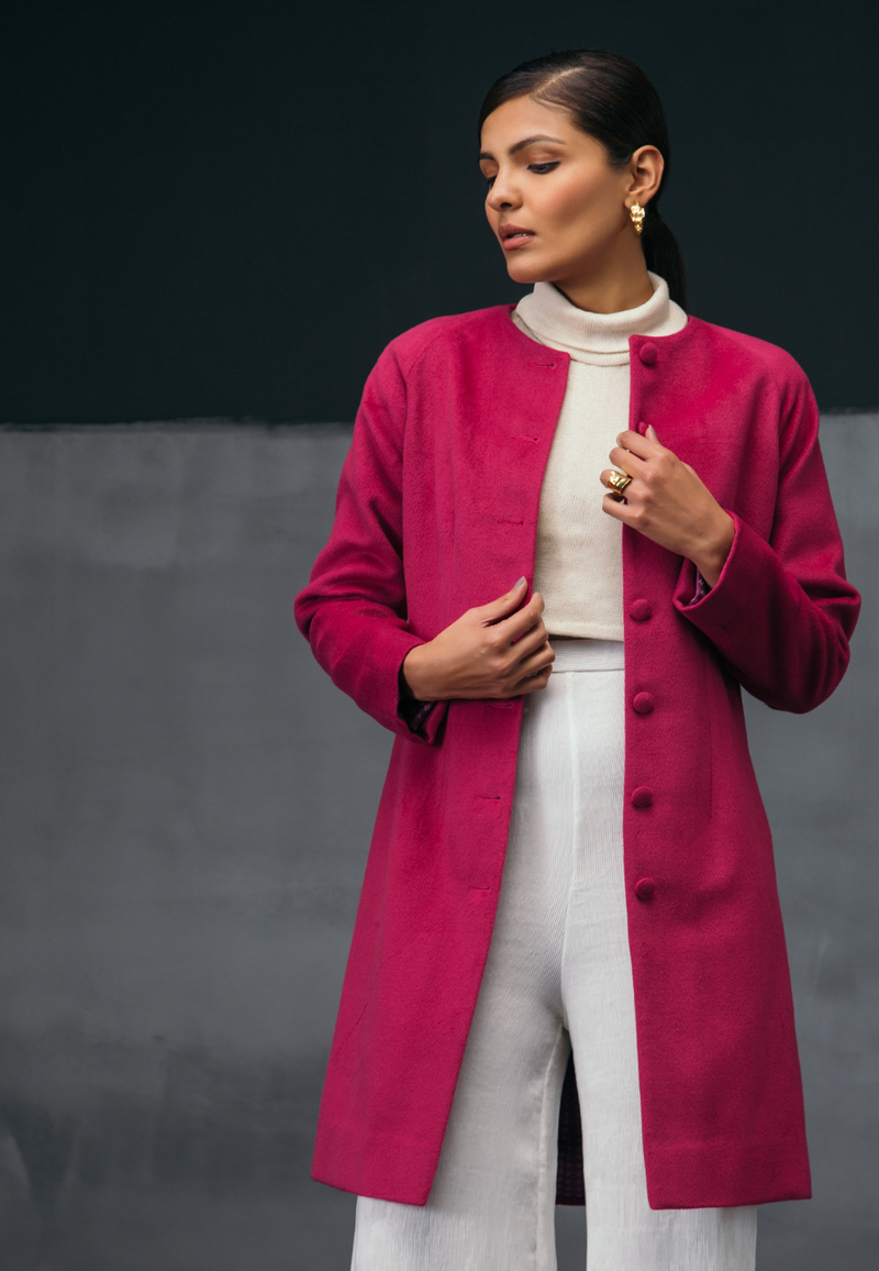 Mannat Gupta's collection of women's jackets and coats. This collarless pink wool coat features wool buttons as closures on the front. It has long sleeves and is cut right on the knee. It the perfect coat for breezy winters. You can wear it to work or for your next dinner plan with girlfriends. Pair it with straight pants and a cropped sweater along with pumps to complete the look.