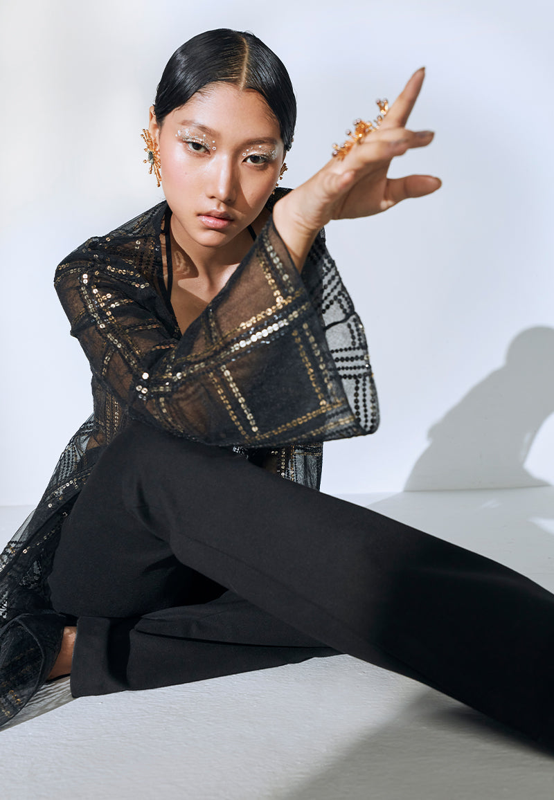 Good for a breezy summer evening or a dinner, this hand-embroidered loose-fit black net jacket is one timeless piece that you can pair with almost anyything. This knee-length jacket features long, flared sleeves and checkered embroidery with rustic gold and black sequins in different sizes. Wear it over a dress or a co-ord set for dinner or even over a swimsuit at the beach or a beach party.