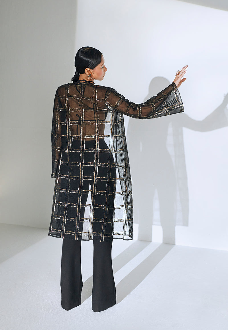 Good for a breezy summer evening or a dinner, this hand-embroidered loose-fit black net jacket is one timeless piece that you can pair with almost anyything. This knee-length jacket features long, flared sleeves and checkered embroidery with rustic gold and black sequins in different sizes. Wear it over a dress or a co-ord set for dinner or even over a swimsuit at the beach or a beach party.