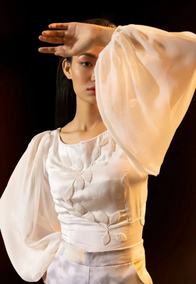 Mannat Gupta's collection of tops for women. This white bodycon top is made using silk and chiffon. The top features a round neck and leaves embroidery on the front with white beads. The long puffed sleeves of the top are made using chiffon to add volume. This versatile, comfortable and minimal blouse can be worn with anything: pants, jeans, skirts, shorts, etc. It is perfect for an elegant date night.