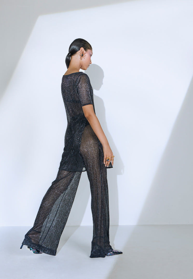 Made from pleated knit fabric, this loose-fit ensemble sets the mood for the summer. The transparent set features an airy, long top with waist-high slits on both sides. The boat neck top comes with a pair of high-waisted, straight pants with slash pockets on both sides. This lightweight blue-black knit set is an easy ready-to-wear ensemble for any party. The iridescent set comes with a black knit bralette. Finish the look with heeled sandals, sneakers or pumps and your favorite jewelry.