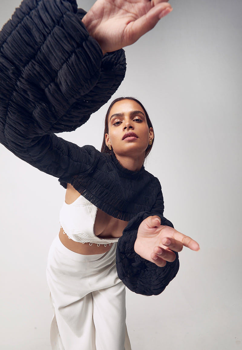 This black puff pleated bust cut crop top is single layered net covered in minuscule handcrafted pleats with elastic thread. The top features ruching detail on the neck with a concealed zip closure. Style it in summers or winters with our white pleated detachable bodysuit and high-waisted pants or our sweetheart tucked mini dress.