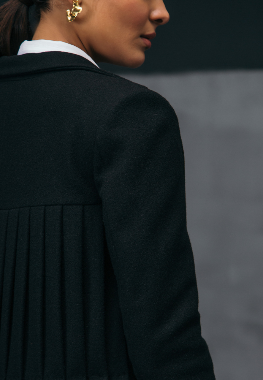 Mannat Gupta's collection of women's coats and jackets. This black collared wool coat comes with pleating on the back creating depth and movement in the piece. The wool coat is floor-length making it perfect to be paired with long dresses and formal attire in the fall and winter. Pair this with a flared pant and top or sweater along with booties and minimal gold jewelry to complete the look 