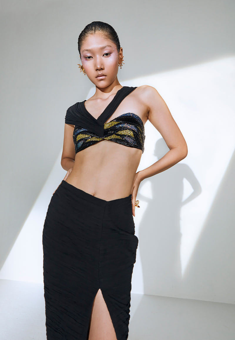 Ruched in lightweight black georgette, this bodycon skirt features an interesting asymmetrical V-shaped waist cut. This black maxi skirt has a zip closure on side seam with a thigh-high slit on the front; it falls till the ankle. Pair it with one of our embellished bustiers, heeled sandals and minimal gold jewelry to complete the look.