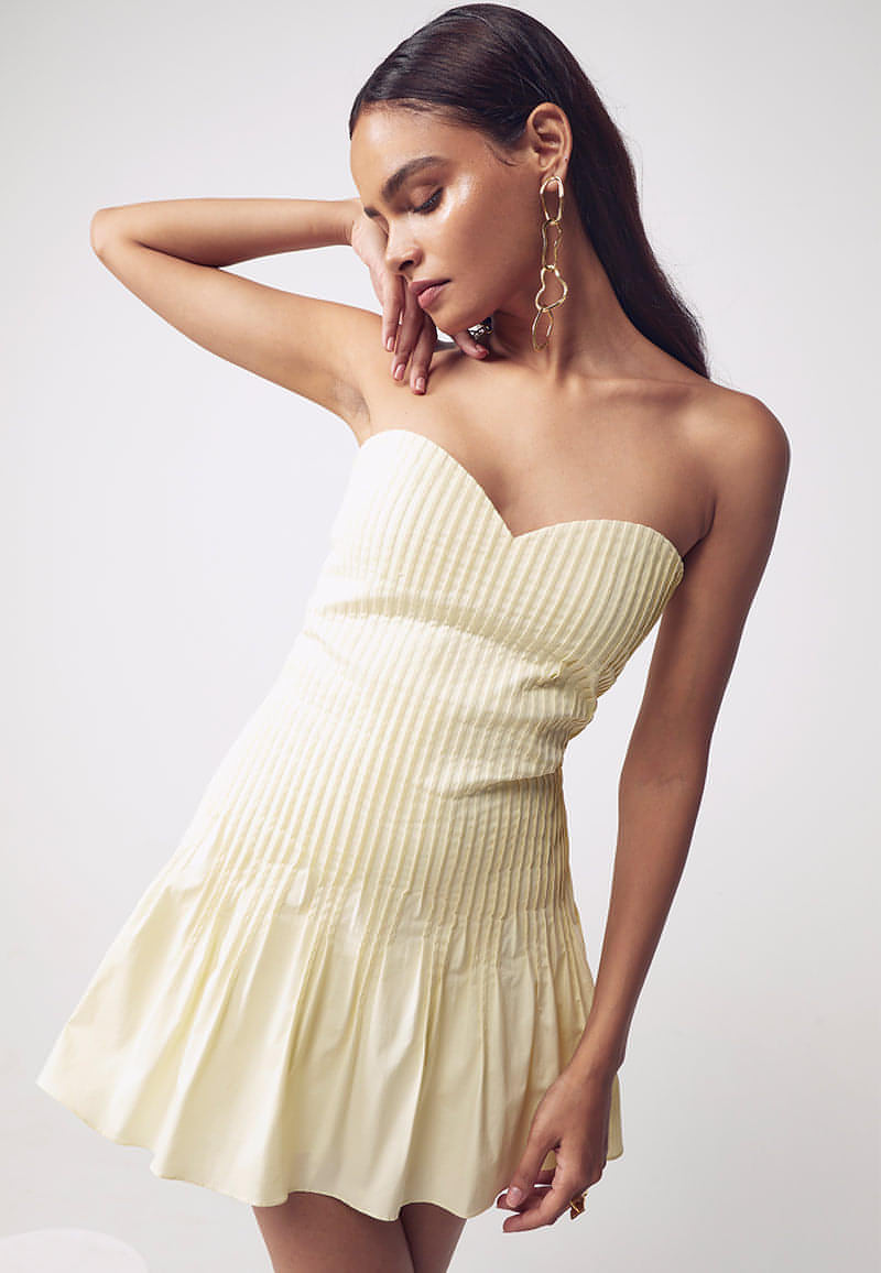 This women's mini dress features couture-inspired details. This buttercream bandeau, bodycon dress features a sweetheart neckline and tuck details on the front for texture and depth, accentuating a woman's body features. This pale yellow mini dress fetures a flared bottom making it perfect for Sunday brunches and birthdays. Pair yours with minimal gold jewelry and heeled sandals to complete the look.